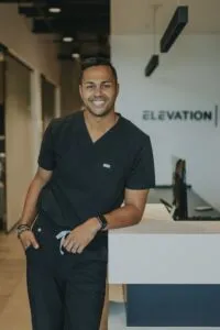 Dr. Brice Gilliam in black scrubs smiling at Elevation Orthodontics reception area, showcasing cosmetic orthodontic expertise.